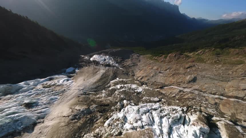 Glacier among mountains reveals exposed terrain and vegetation suggesting ice retreat