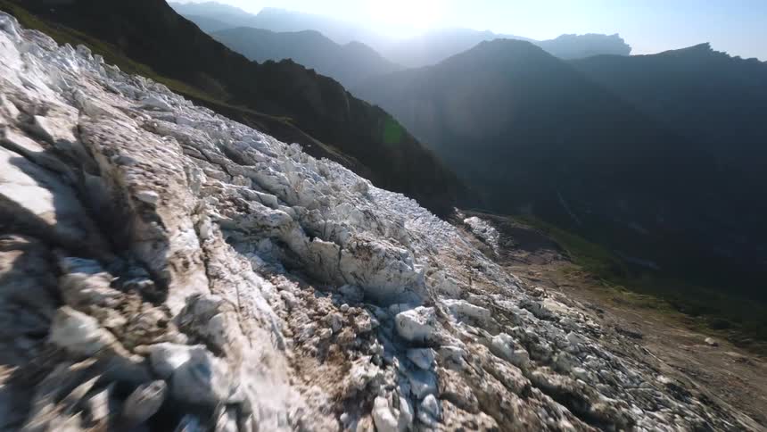Uneven glacier surface lit by the sun with mountain ranges in the background