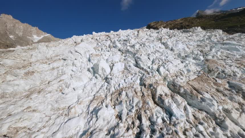 Glacier with rugged surface stretches toward mountain under clear blue sky in alpine setting