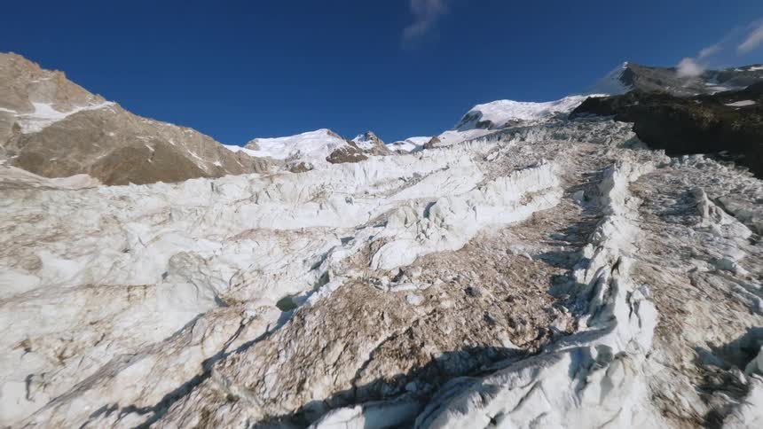 Aerial view of a broad glacier stretching down rugged mountains beneath bright blue skies