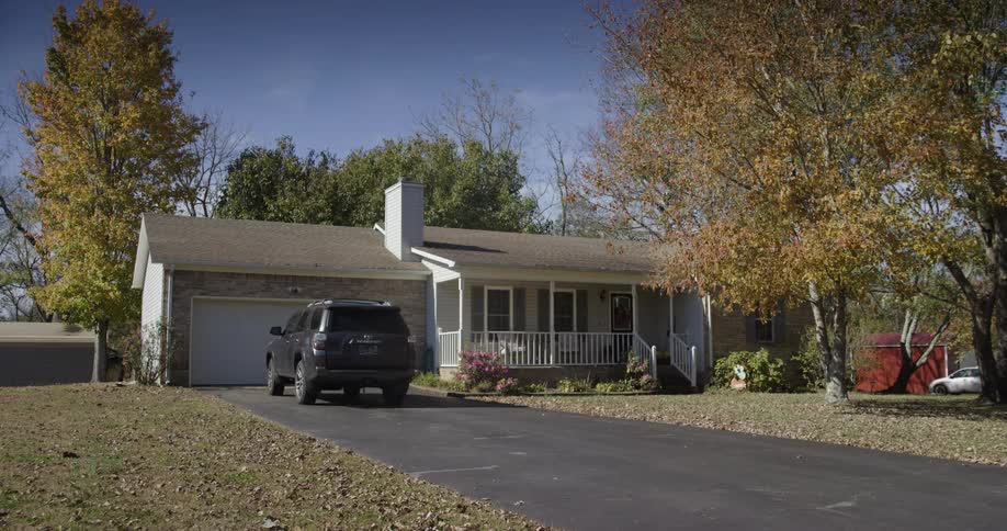 Singlestory house with garage and black suv parked in front surrounded by trees with autumn leaves