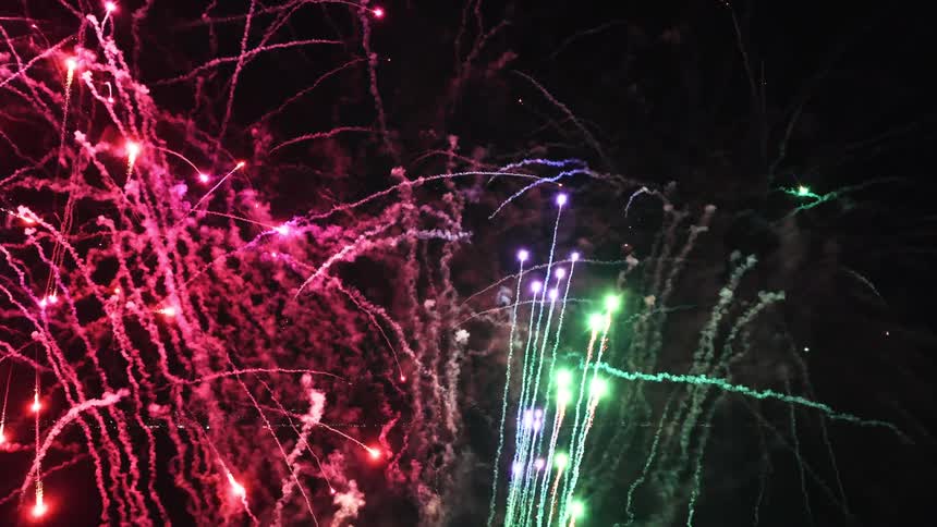 Fireworks glow as they explode and leave smoke trails in the night sky along the coast