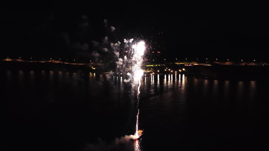 Colorful fireworks explode above floating platform with reflections on water during nighttime
