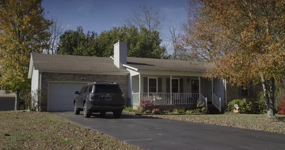 Singlestory residence with garage and black suv at the entrance surrounded by trees with autumn leaves
