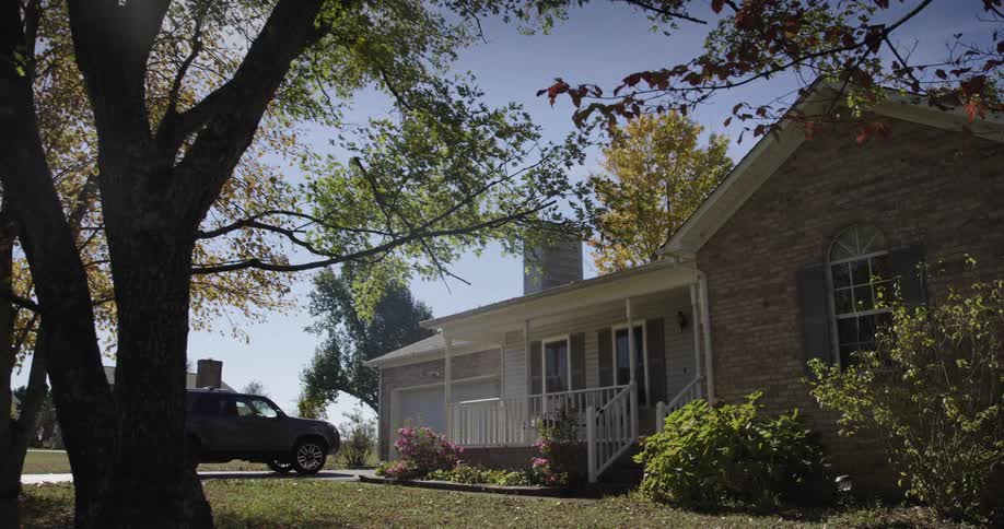 Sunlight shines through the branches of a tree as a truck is parked in the driveway of a neighborhood house