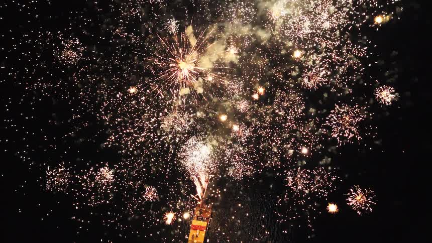 Illuminated boat launches multicolored fireworks exploding in the night sky above the water
