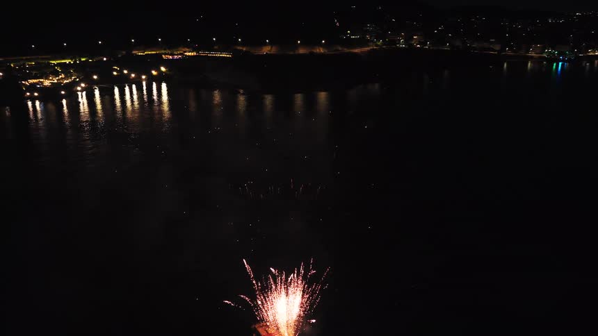 Fireworks coming from a white boat on a body of water with a metropolitan city on the background outdoors during night time