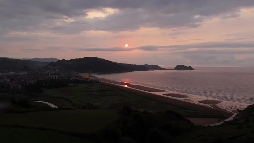 Beach with the ocean to one side and green land to the other outdoors during dusk or dawn