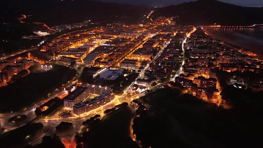 Coastal city lit at night displays gridpatterned streets with beach reflecting urban lights