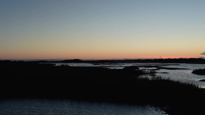 Low vegetation surrounds body of water under orange sky at sunrise or sunset