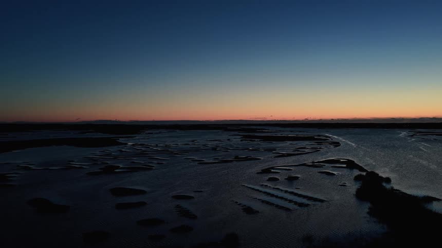 Horizon in blue and orange tones over wide flooded areas with exposed sandbanks
