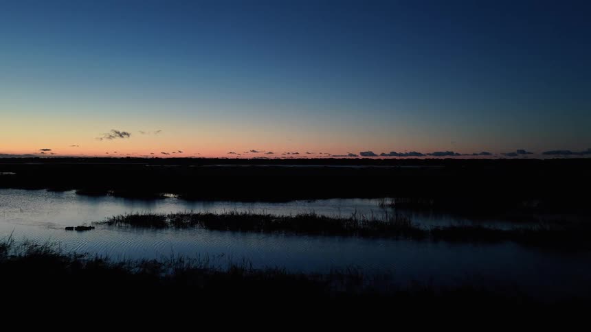 Water reflecting blueorange twilight sky surrounded by dark vegetation and low clouds