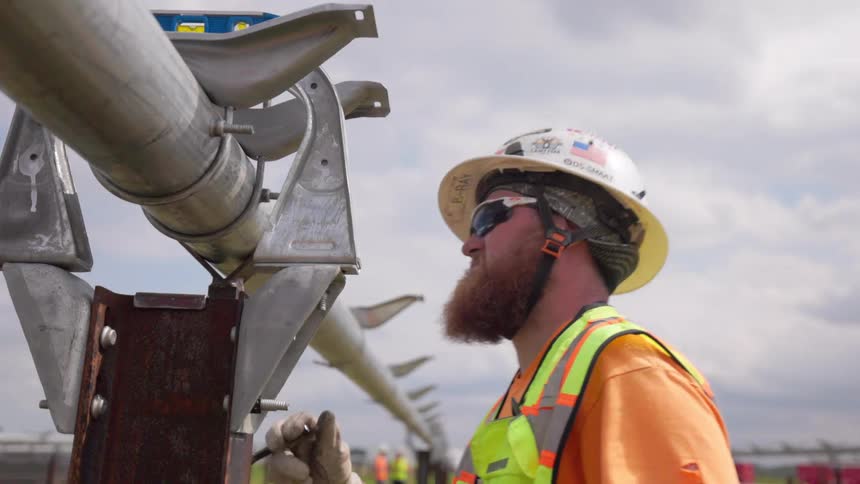 Construction worker wearing sunglasses using pliers to screw a structure outdoors during day time