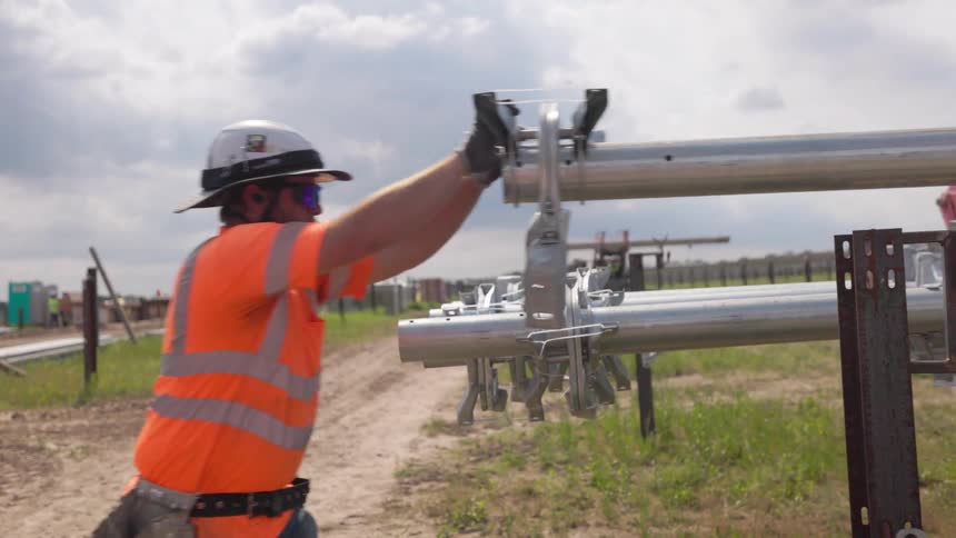 Worker adjusts metal brackets on cylindrical pipes in outdoor installation area