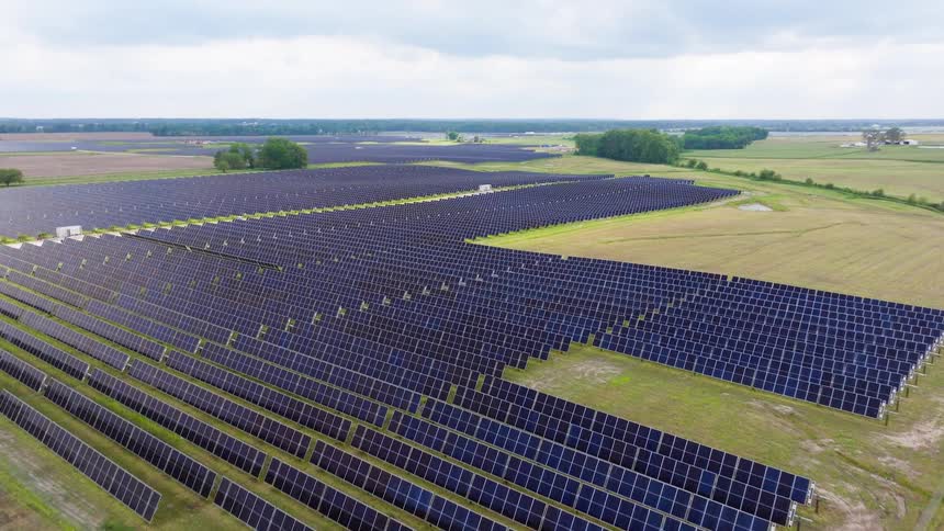 A solar farm filled with panels stands on a grassfield at midday