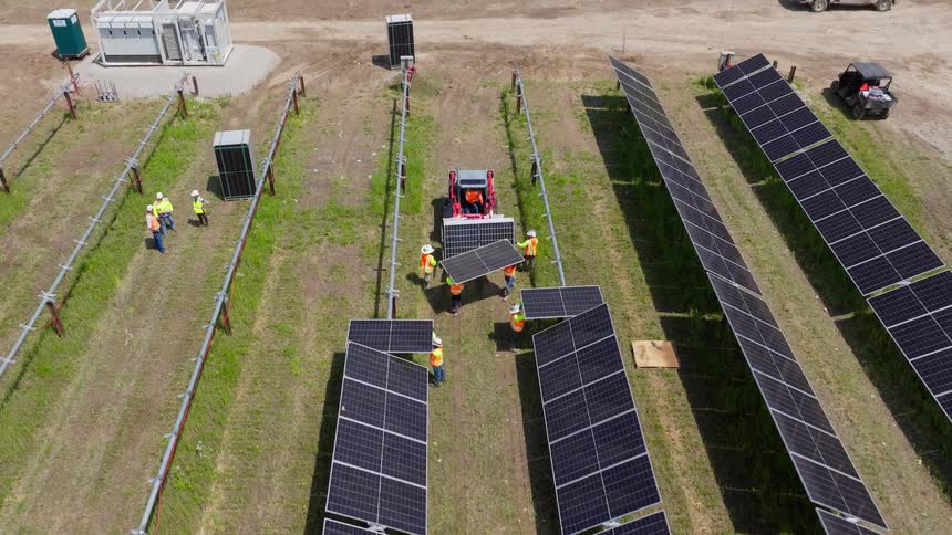 Workers installing rows of solar panel on the middle of a field outdoors during day time