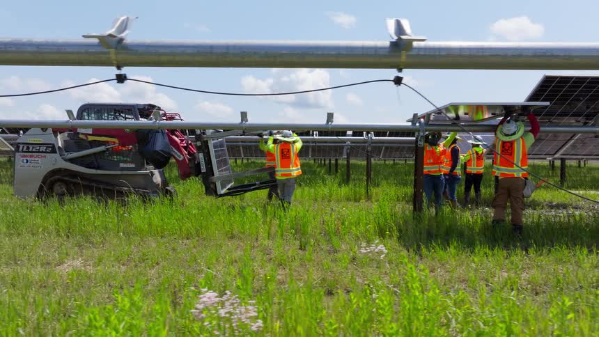 Employees are placing solar panels on metal structures on a solar farm