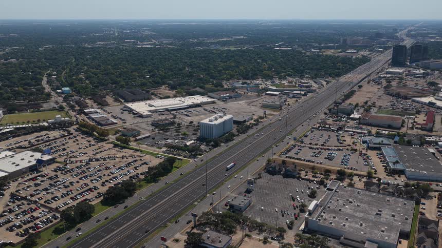 Wide highway running through an urban area with parking lots businesses and neighborhoods spread around