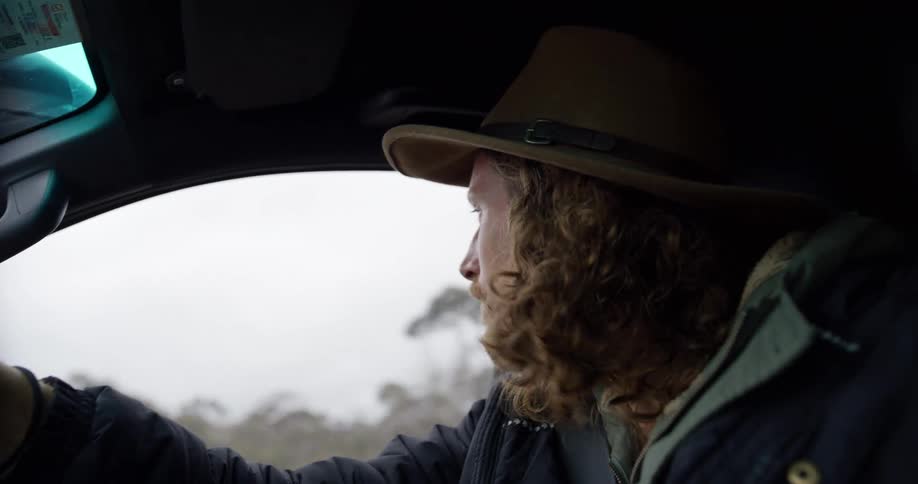 Man wearing a hat driving a vehicle with a blurred landscape in the background