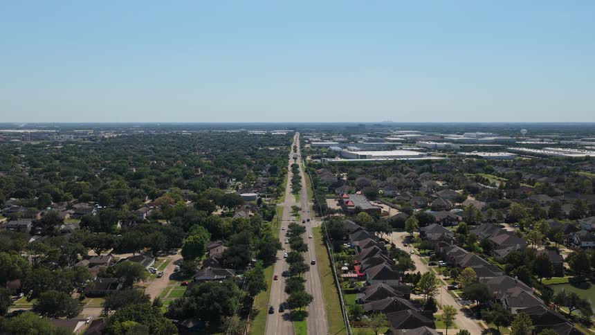 Long avenue bordered by residential neighborhoods and wooded areas seen from above
