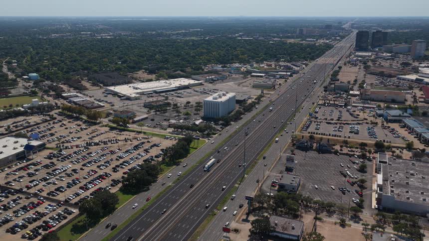 Wide highway seen from above surrounded by parking lots commercial buildings and wooded areas