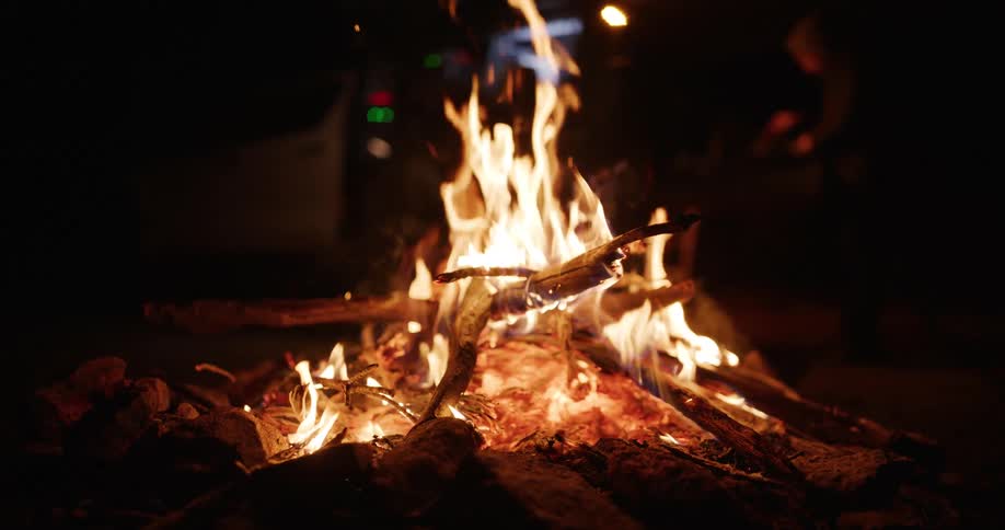 Intense campfire with burning logs surrounded by stones at night