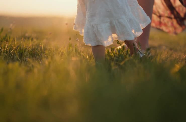A little girl in a white dress next to an adult walking on a green lawn