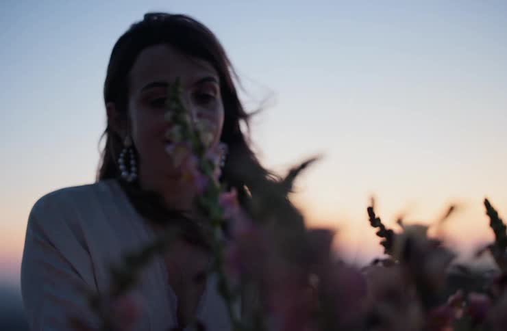 Darkhaired woman in a closeup at dusk with blurred plants in the foreground