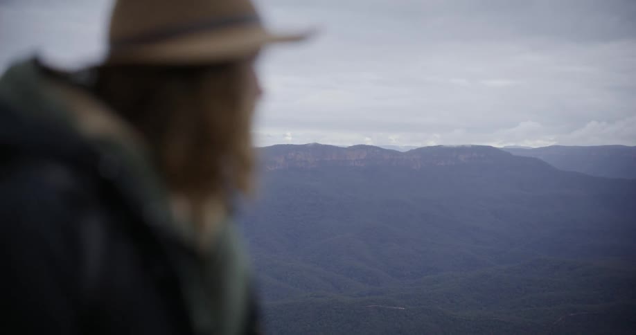 Person wearing a hat photographing a mountain landscape with a longlens camera