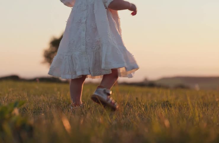Child in a white dress walking through the grass at dusk