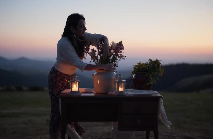 Woman arranges flowers in ceramic vase on outdoor table at sunset