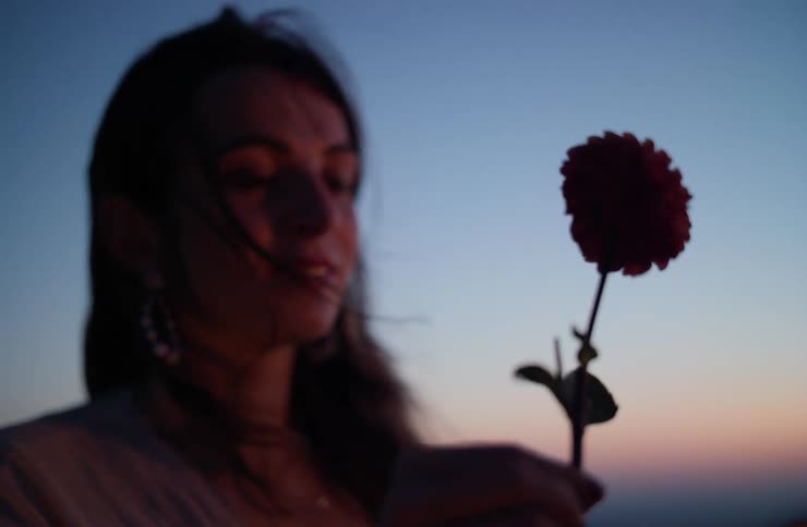 The face of a young woman looking at a flower in her hands in an outdoor setting