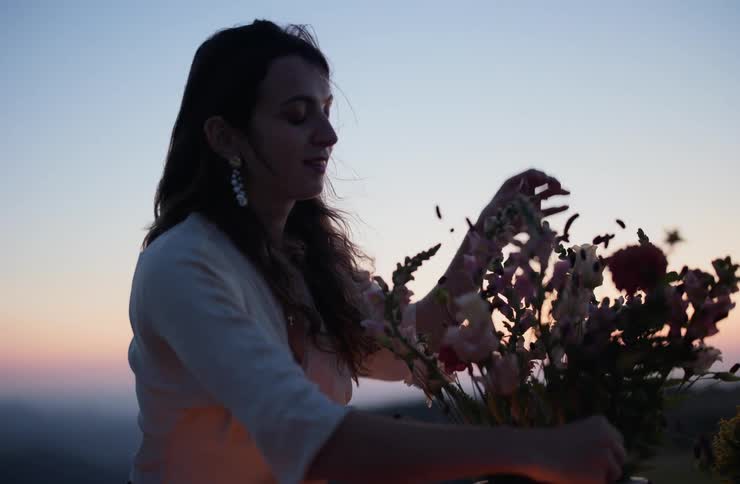 A woman is smiling as she places a flower in a bouquet