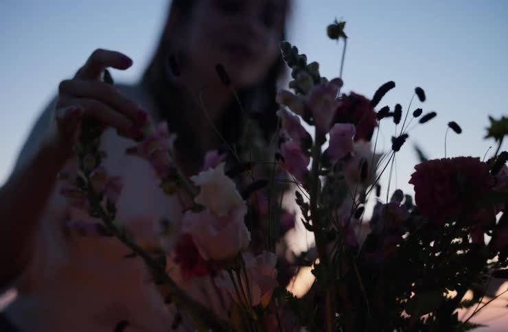 A woman gently arranges a vibrant bouquet of flowers her silhouette framed against the warm fading light of a sunset sky
