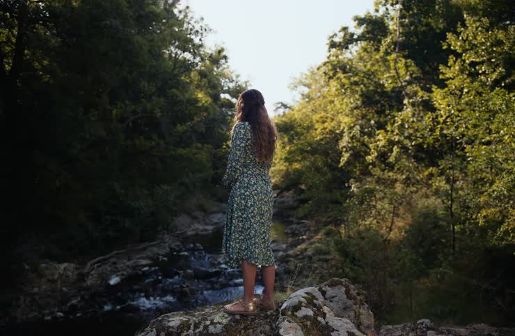 Young woman stands on rocks overlooking a stream in the forest