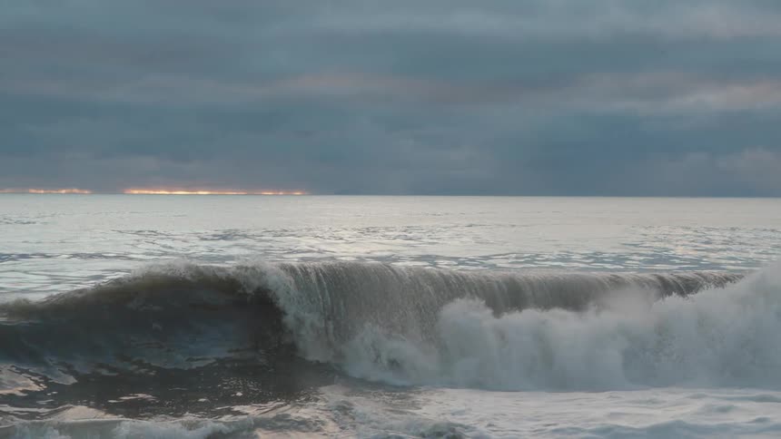 Wave forming in the sea under a cloudy sky with a band of light on the horizon