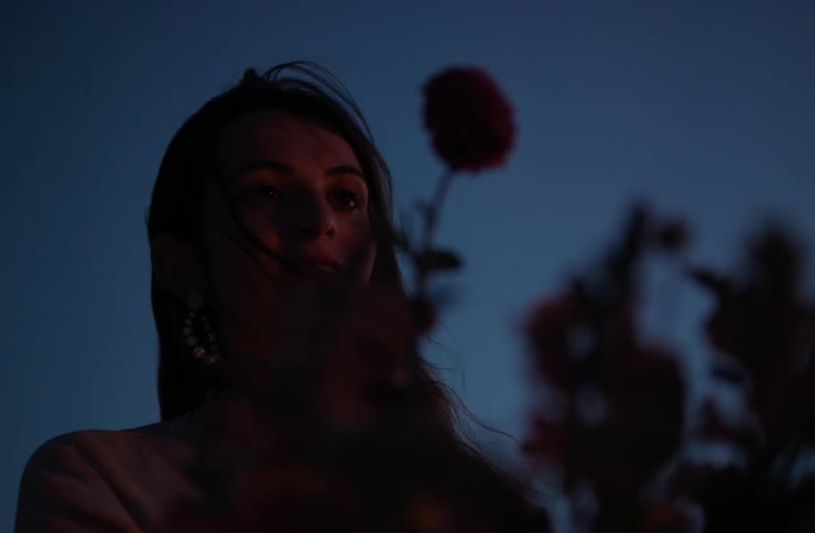 Partially lit woman holding a flower with a dark blue evening background