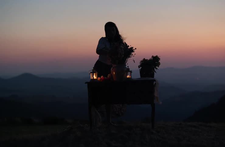 Silhouette of a woman in front of a table with lanterns and flowers on a hillside at dusk
