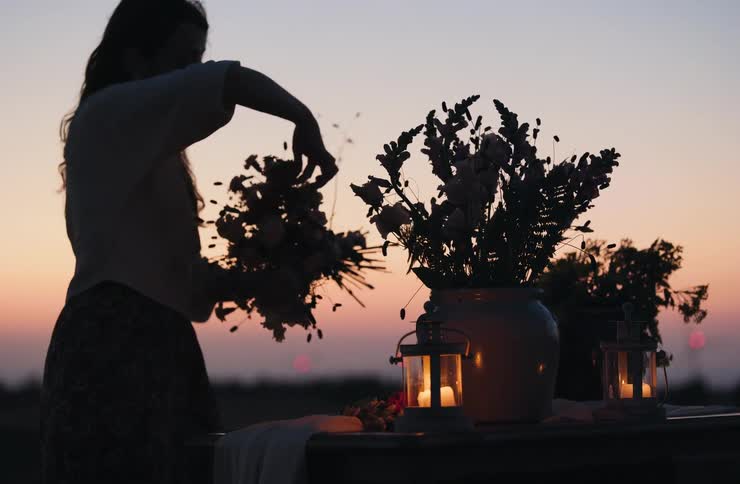 Silhouette of a woman assembling a floral arrangement on a table with lanterns at sunset