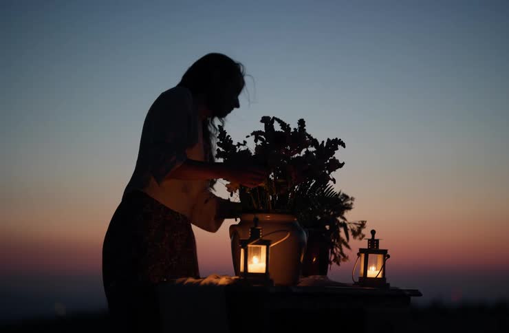 Silhouette of a woman arranging flowers on a lanternlit table at dusk