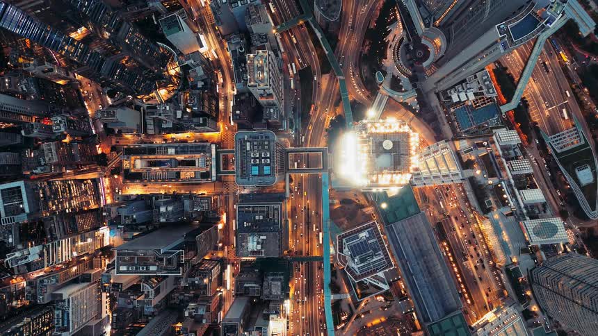 Aerial view of city lit at night with tall buildings and heavy traffic