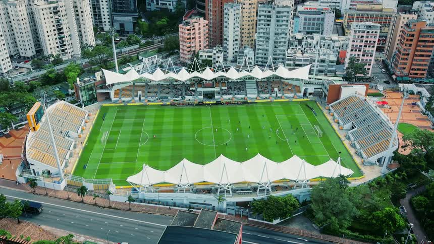 Aerial view of a downtown soccer stadium surrounded by buildings as players run on the field and traffic moves on the highway