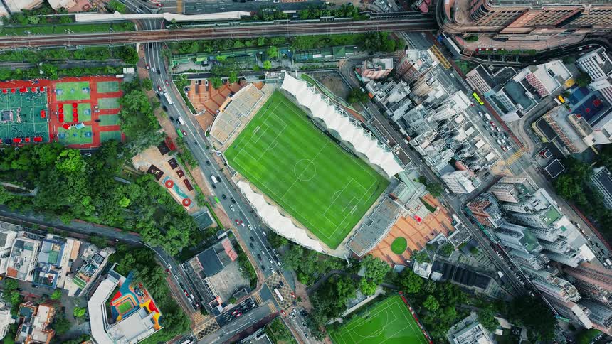 Aerial view of a downtown soccer stadium surrounded by buildings as players run on the field and traffic moves on the highway