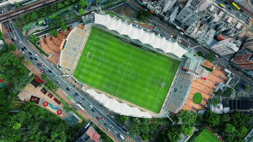 Aerial view of a downtown soccer stadium surrounded by buildings as players run on the field and traffic moves on the highway