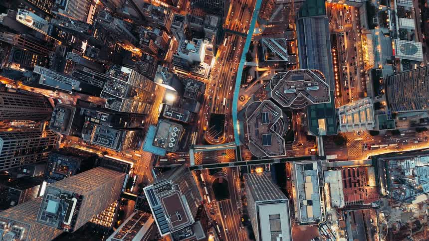 Traffic flows through a dense grid of illuminated streets and skyscrapers at night