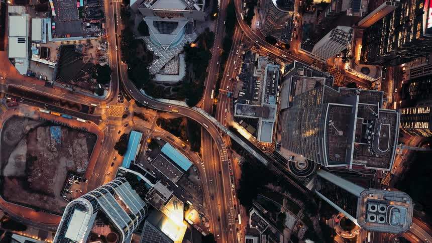 A top down aerial view captures the glowing highways and traffic weaving through a dense city at night