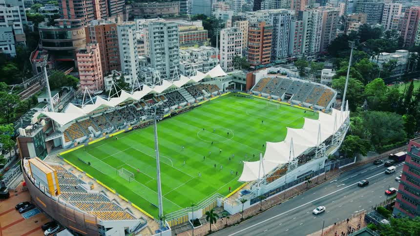 Aerial view shows football stadium surrounded by tall buildings and busy roads in urban area