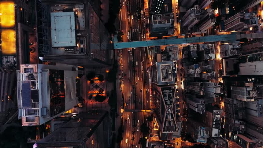 This is a dramatic highangle aerial video of a dense urban center at night looking straight down onto city streets and towering skyscrapers the main focus is the bright golden light illuminating the roadways which are busy with the movement of traffi