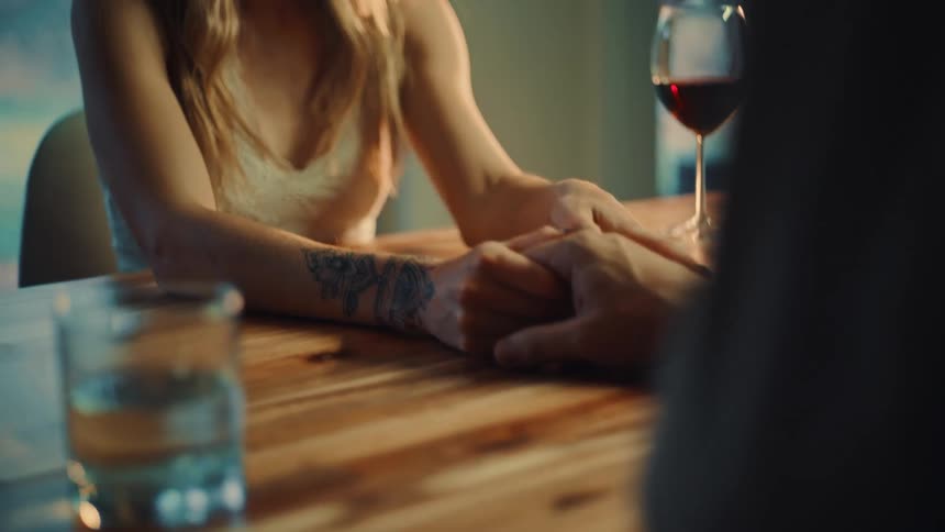 Interlocked hands on a wooden table with a glass of wine and a glass of water nearby
