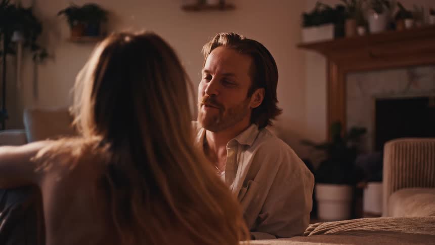 Man smiling while talking with a woman as they sit in a softly lit living room